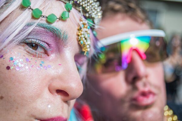 Zwei Menschen mit glitzernd-bunt verzierten Gesichtern auf einem Festival.