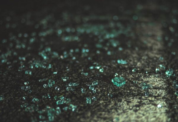 Auf einem dunkelgrünen Untergrund liegen winzig kleine, im Licht türkis schimmernde Glasscherben wild herum.
