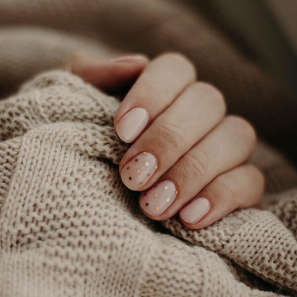 Eine Frauenhand, deren Nägel mit goldenem Motivglitzer in Kreisform dekoriert sind, hält den Saum eines Pullovers.