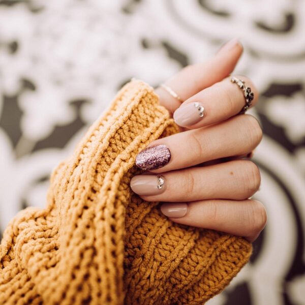 Die Nägel einer Frauenhand sind mit lilafarbenem Glitzernagellack und Strasssteinen verziert.