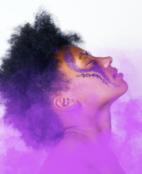 Eine Frau mit violettem Festival-Make-Up steht in einem lila Rauch