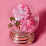 In einer Glaskugel befindet sich eine rosa Rose mit goldenem Glitzer ringsherum