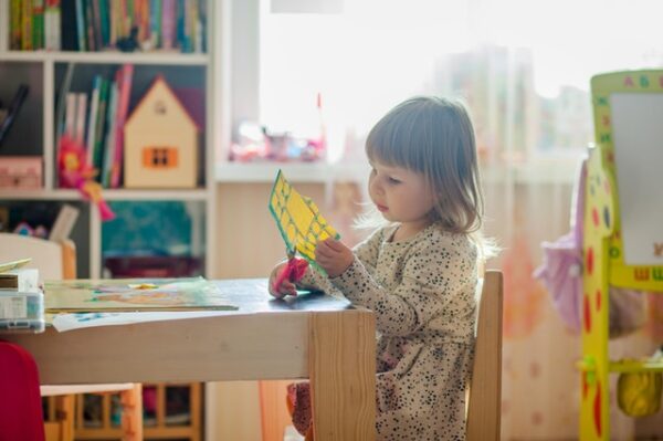 Ein kleines Mädchen sitzt an einem Tisch und zerschneidet ein Blatt Papier
