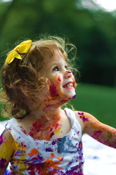 Ein kleines Mädchen voller Farbflecken sitzt auf einer Wiese