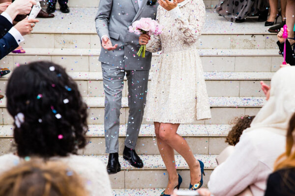 Ein Hochzeitspaar steht auf einer Treppe, die Gäste streuen Glitter