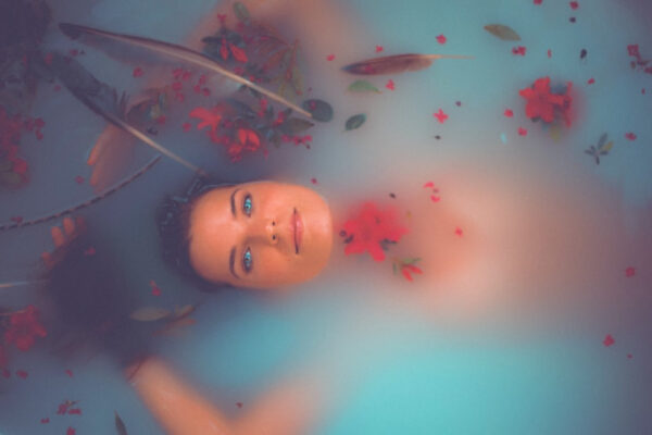 Eine Frau liegt in einer Badewanne mit milchigem Wasser umgeben von roten Blüten