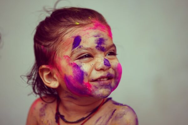 Ein junges Mädchen, das im Gesicht pinke und lila Farbklekse hat, grinst.