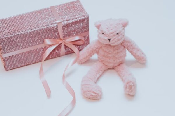Ein Geschenk ist in pinkem Glitzerpapier eingeschlagen, daneben sitzt ein Teddybär