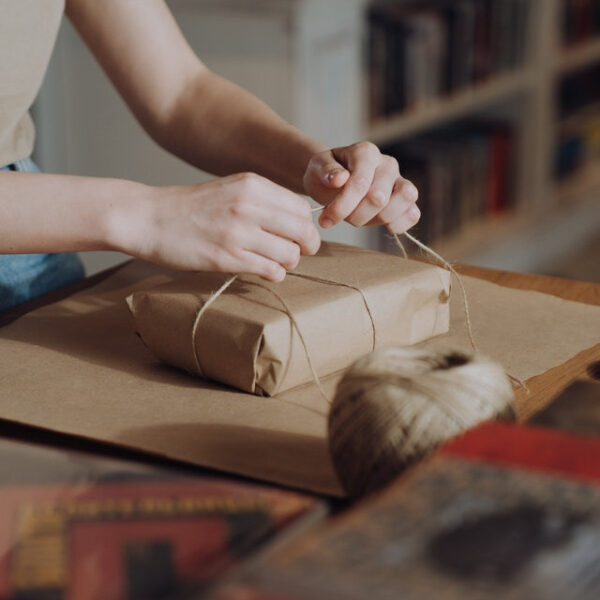 Jemand verpackt ein Geschenk in Packpapier und umwickelt es mit einer Kordel