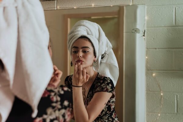 Eine Frau mit einem Handtuch um dem Kopf schaut sich im Spiegel an