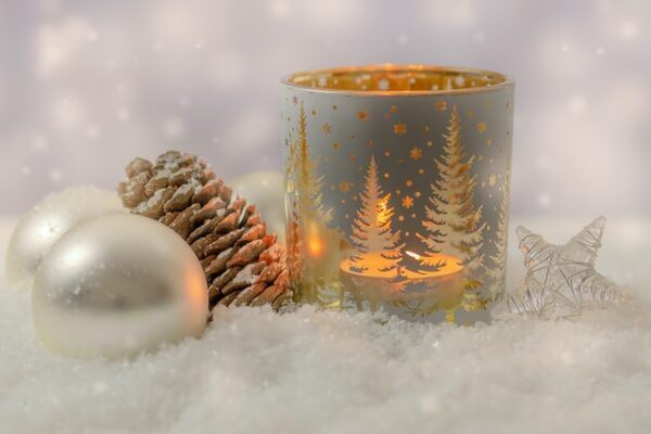 Ein Teelicht mit Mustern aus Bäumen, daneben zwei Weihnachtskugeln und ein Tannenzapfen