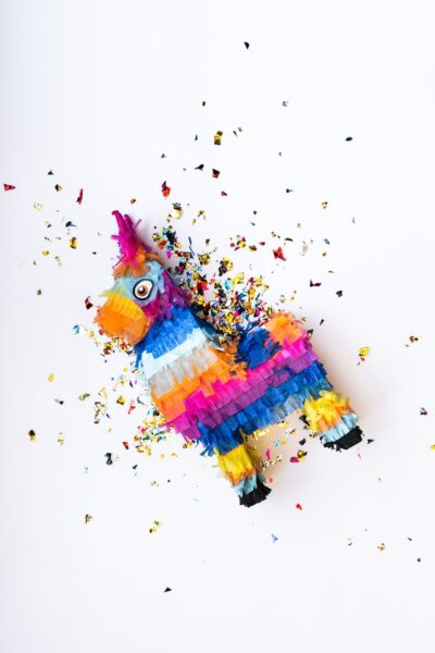 Eine bunte Piñata in Form eines Pferds liegt auf einem weißen Untergrund. Drumherum ist viel Konfetti und Glitzer verstreut