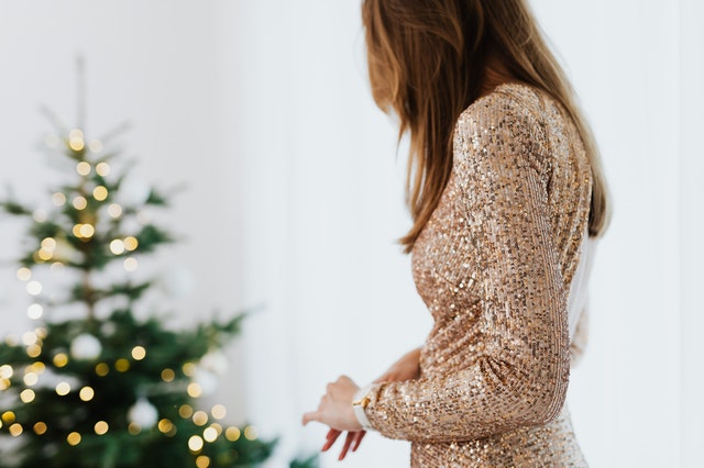 Eine Frau mit einem goldenen Glitzer-Kleid steht vor einem Weihnachtsbaum