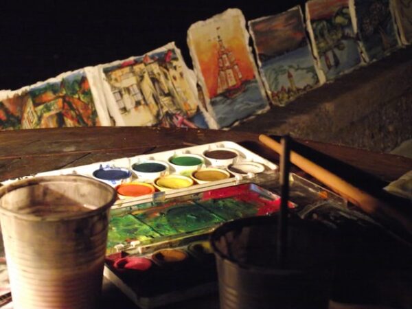 Ein benutzter Farbkasten mit kleinen gemalten Bildern im Hintergrund